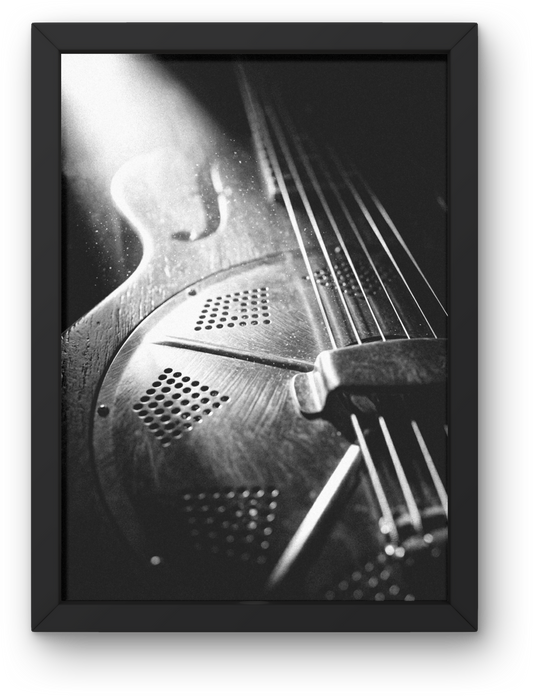 Close-up of a resonator guitar's soundhole and strings in black and white, framed.
