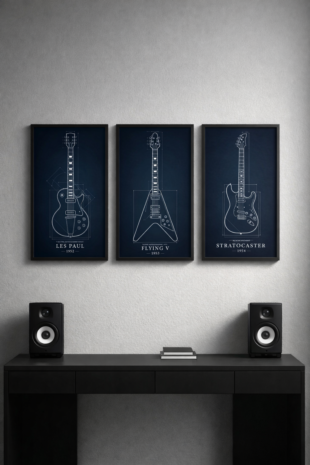 Three framed guitar blueprints on a wall above a desk with speakers.