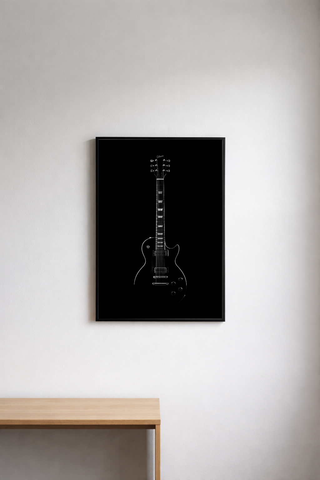 Framed gibson les paul guitar on a white wall above a wooden table